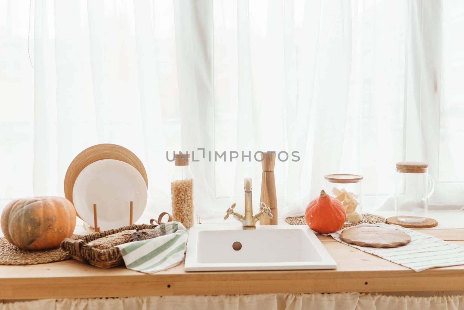 Kitchen countertop by the window in a bright room. Orange pumpkins, bread and pasta on the countertop. Autumn mood at home.