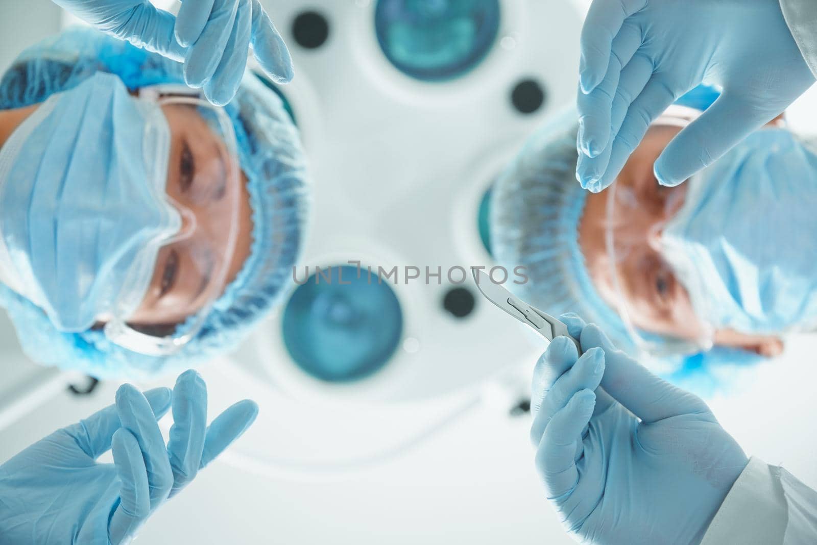 Two surgeons in protective uniform preparing for operation, looking at camera on background of surgical lamp