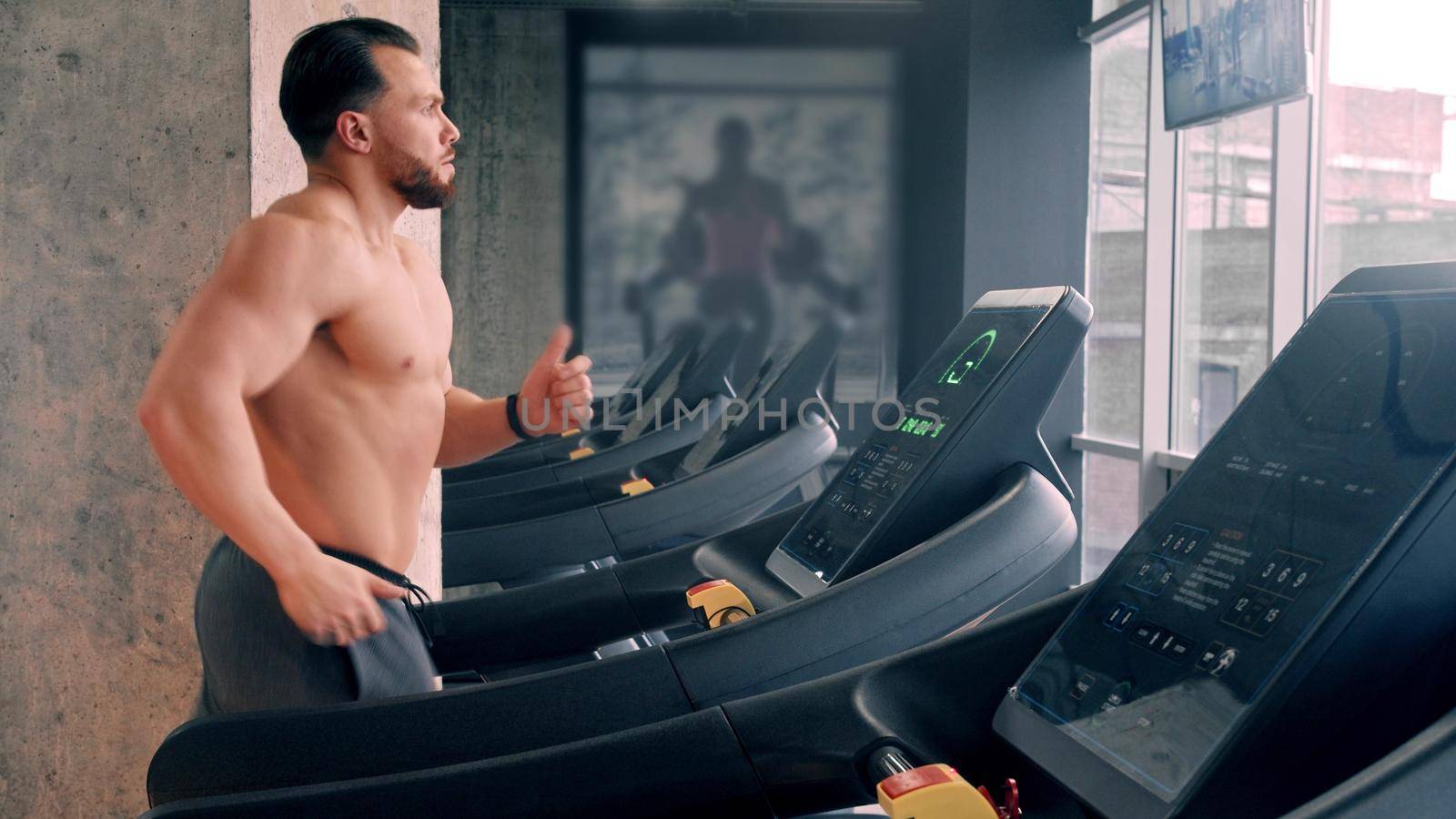A bearded attractive man bodybuilder running on the treadmill. Mid shot