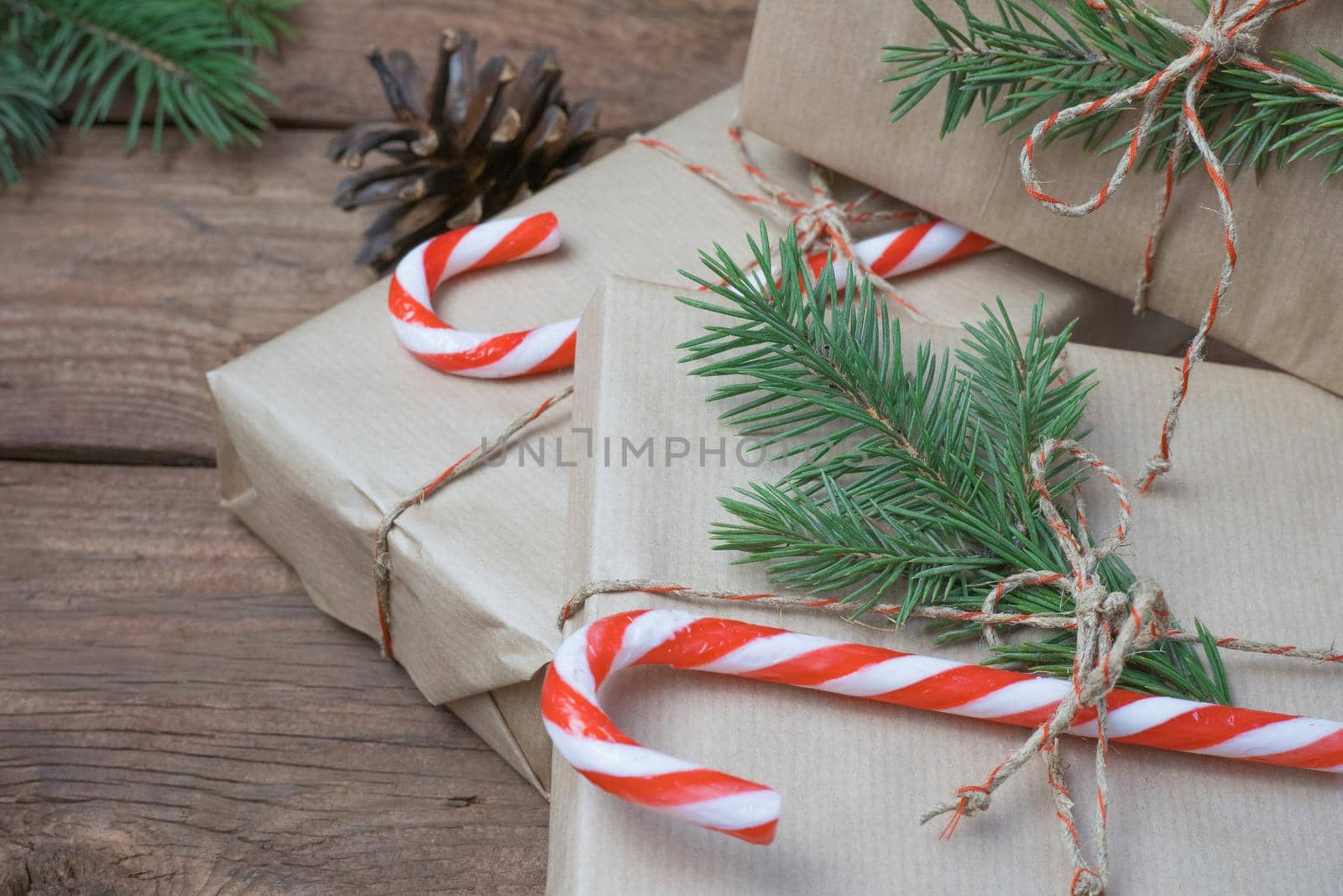 Christmas gifts or gift box wrapped in kraft paper with decorations, pine cones and fir branches on a rustic wooden background