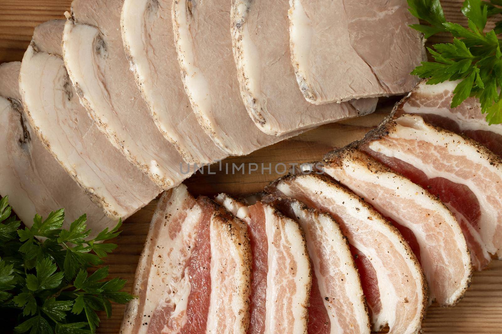 Sliced pork deli meats on wooden platter.