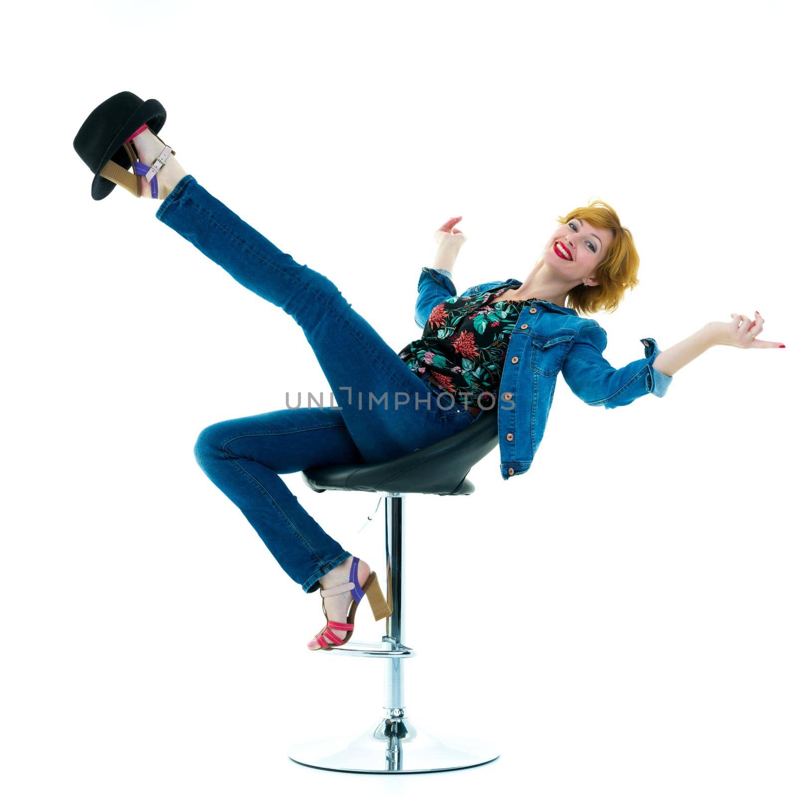 Beautiful young woman posing studio in a bar stool, she put a hat on her leg. Photo joke.