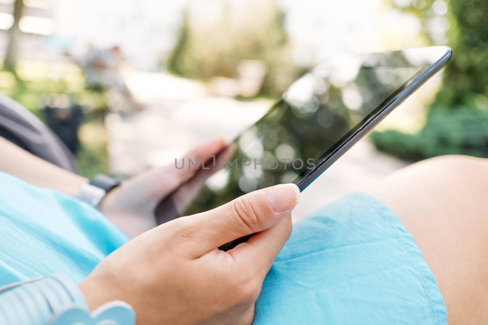 Unrecognizable young woman using digital tablet in the park, close-up of hands.