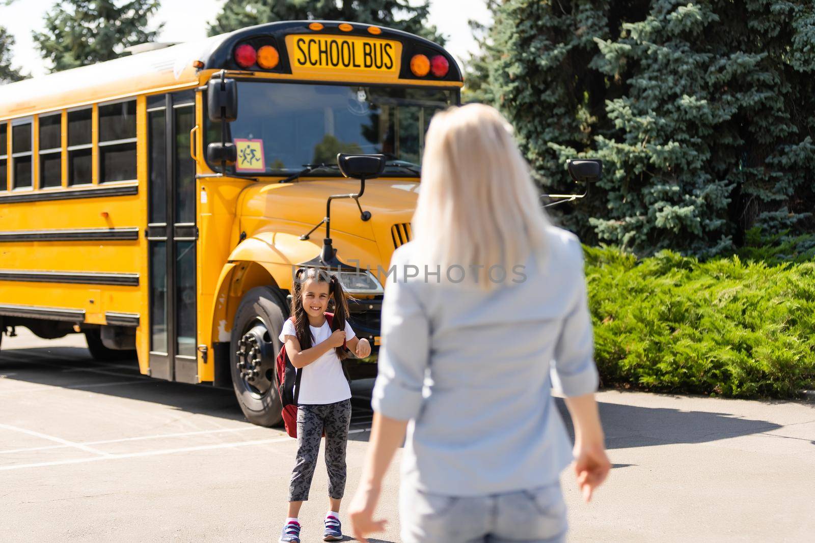 Mother escorts the schoolgirl with ponytails and a backpack to school.