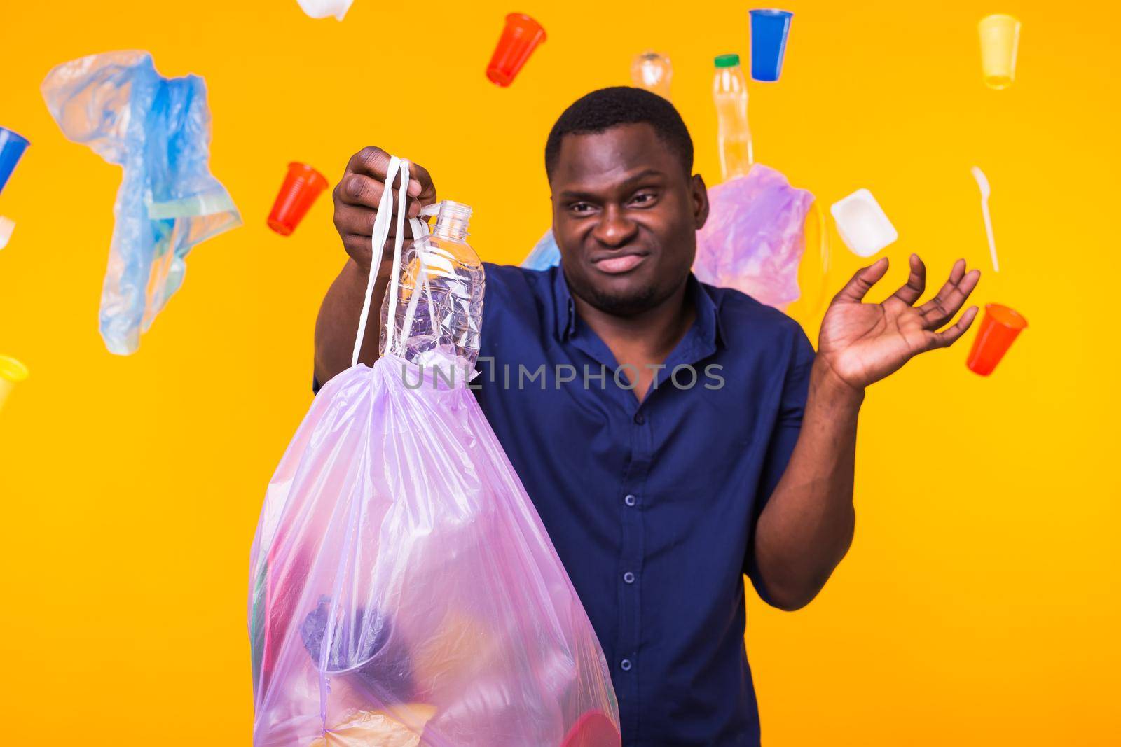 Problem of trash, plastic recycling, pollution and environmental concept - confused man carrying garbage bag on yellow background.