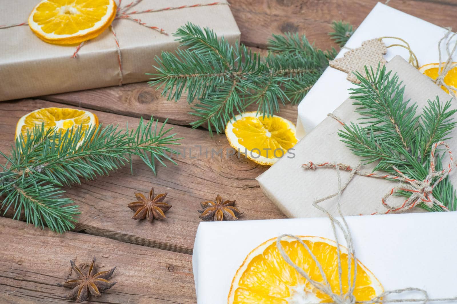 Christmas presents or gift box wrapped in kraft paper with decorations, pine cones, dry orange orange slices and fir branches on a rustic wooden background. Holiday concept.