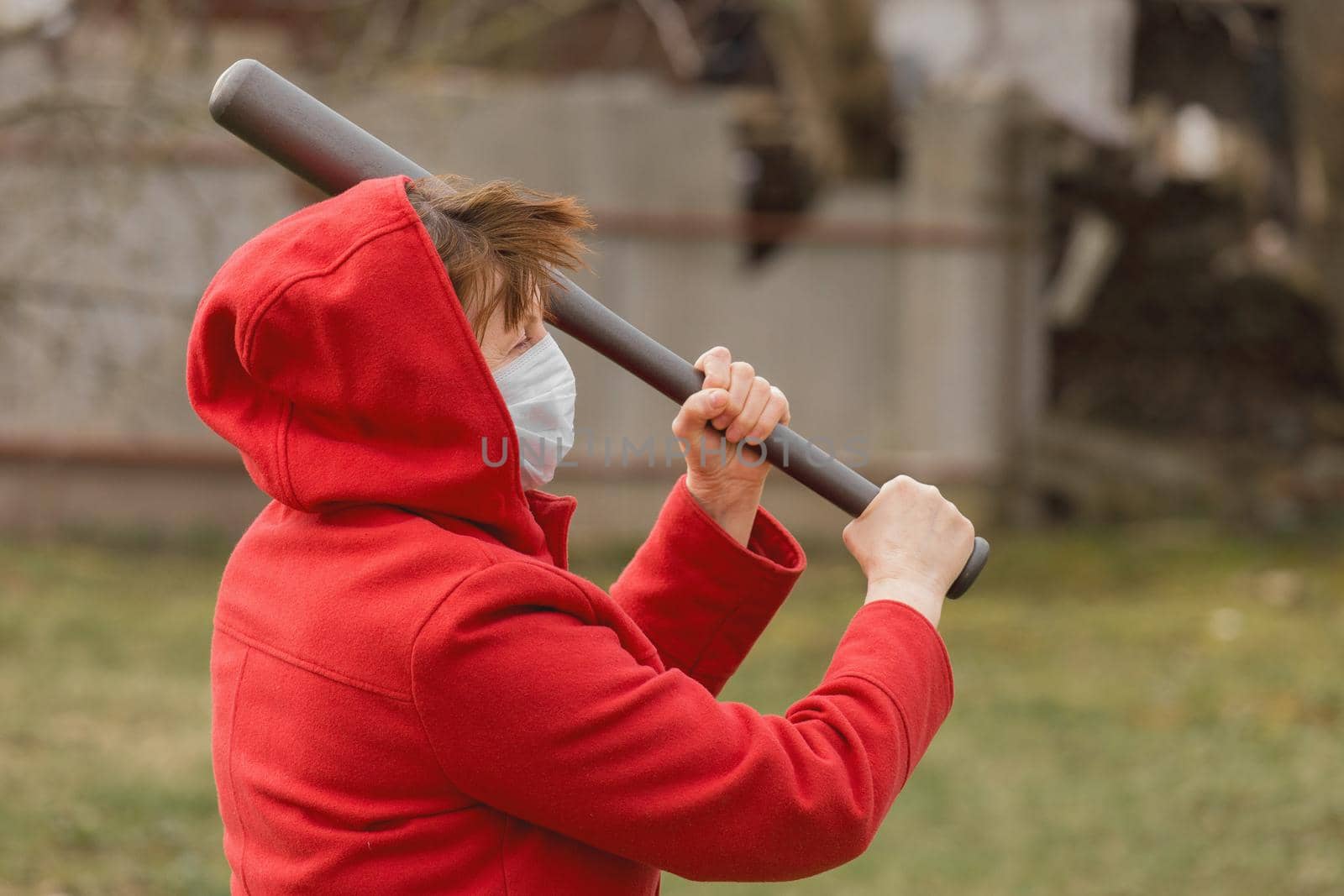 Angry aggressive elderly woman in protective safe medical mask swings baseball bat in the background of outdoor street, portrait, close up.