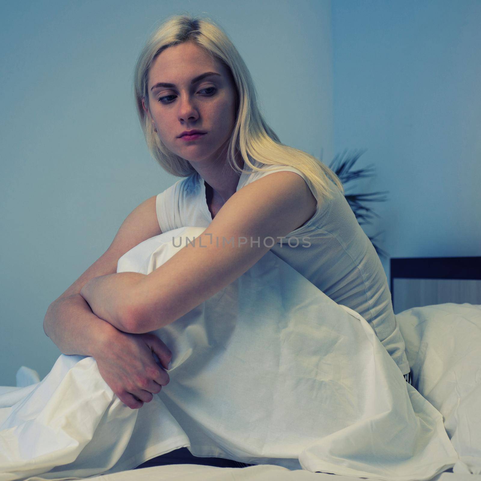 Sad depressed woman sitting in her bed late at night, she is pensive and suffering from insomnia - Image toned