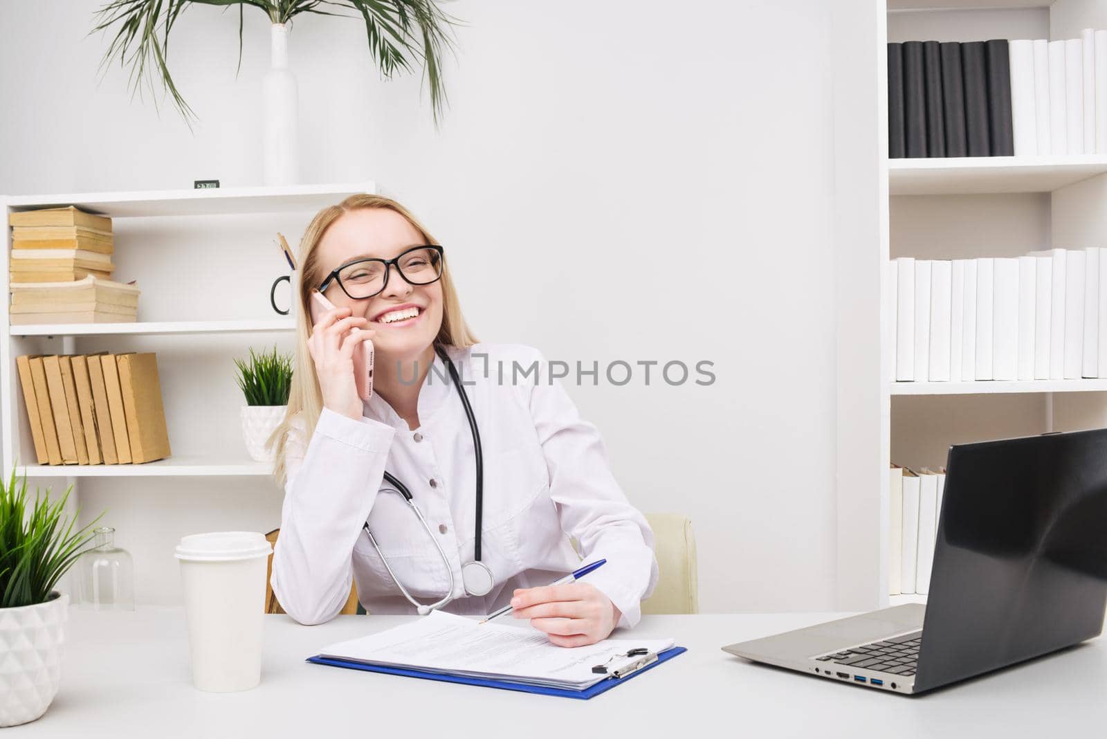 Portrait of a beautiful smiling woman doctor while talking on the smartphone and complete a medical information by zartarn