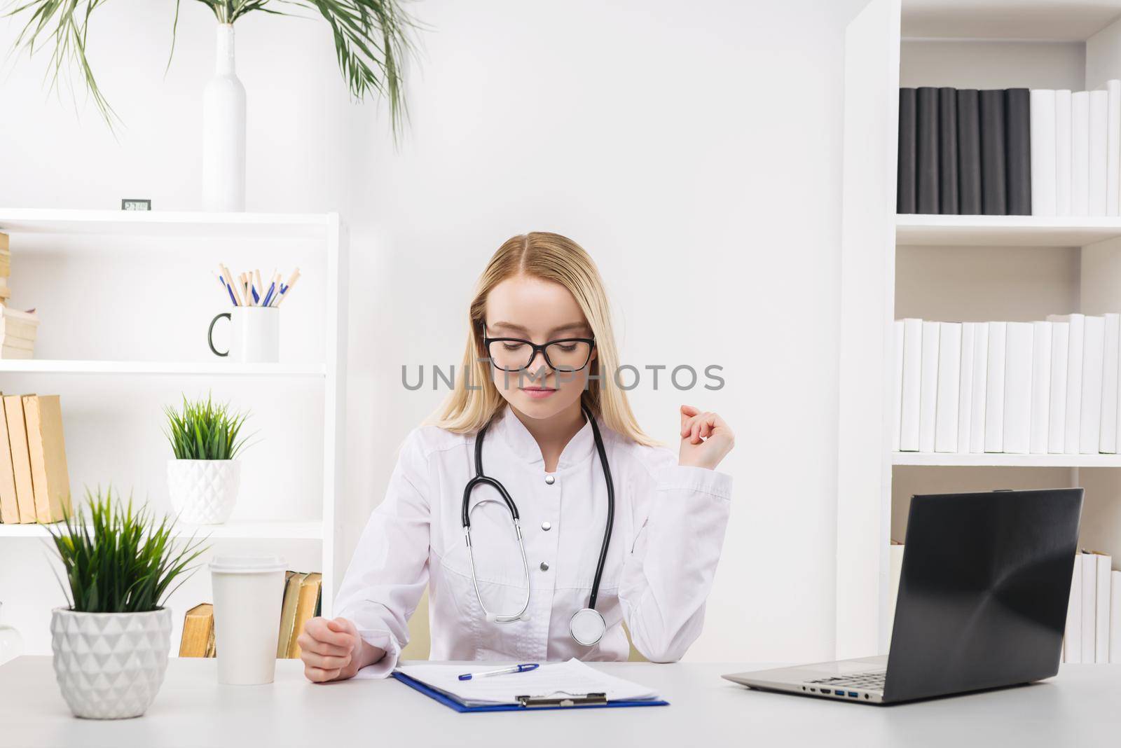 Young beautiful doctor woman working happy and smile in hospital, sitting on table, medical concept