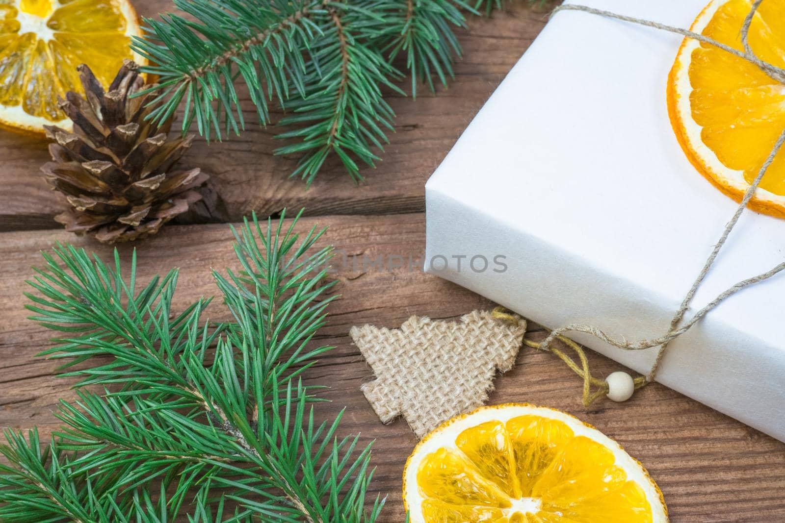 Christmas presents or gift box wrapped in kraft paper with decorations, pine cones, dry orange orange slices and fir branches on a rustic wooden background. Holiday concept