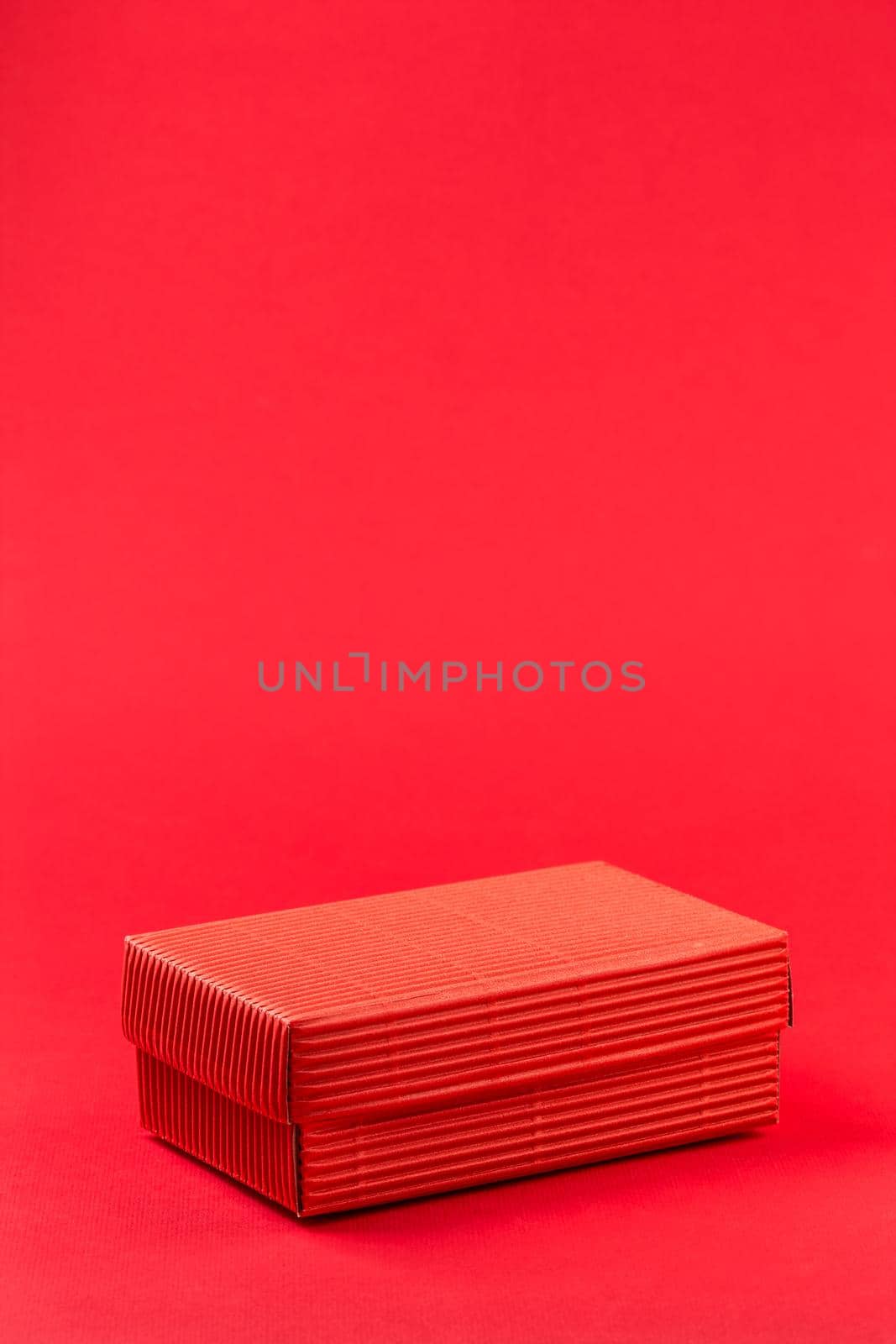Monochromatic photo of red closed corrugated cardboard box on red background. Valentine's Day gift packaging concept