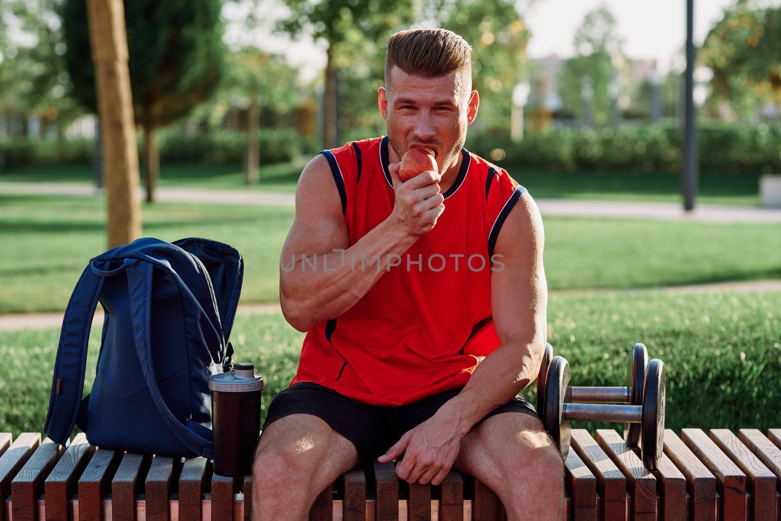 sporty man resting in the park on a bench having a snack by Vichizh