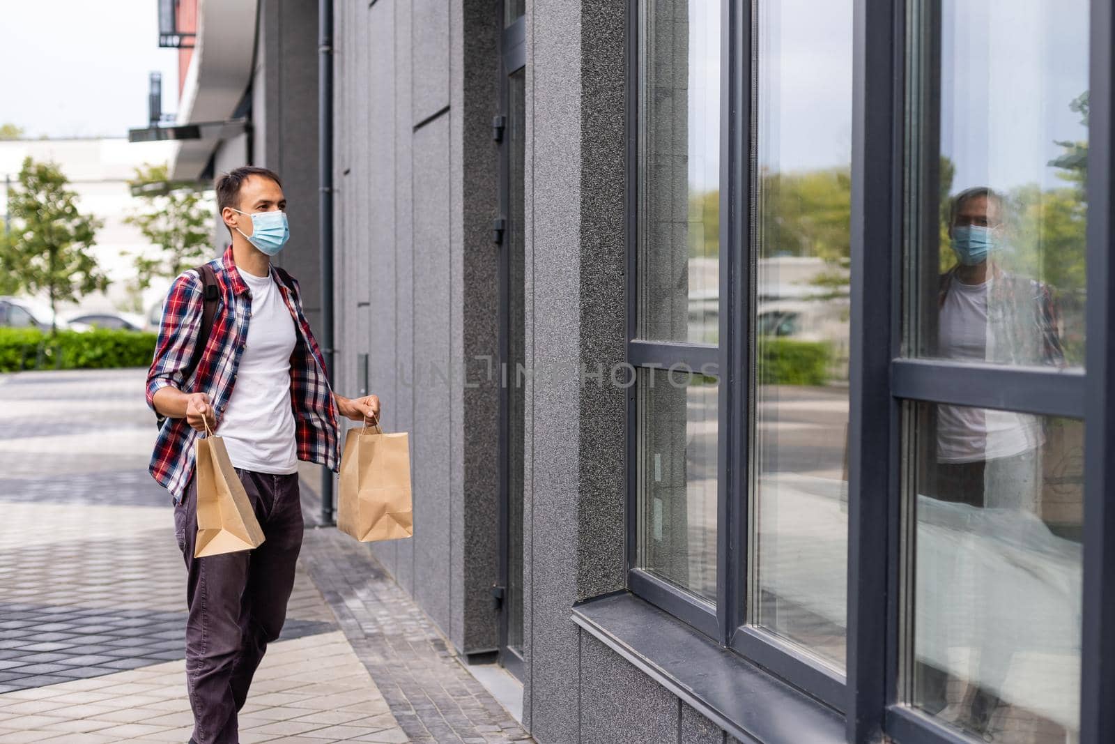 Young delivery man in medical mask on face holding paper bags in hands. Hipster man courier with shopping bags. Safe online delivery service. Coronavirus COVID-19 protection