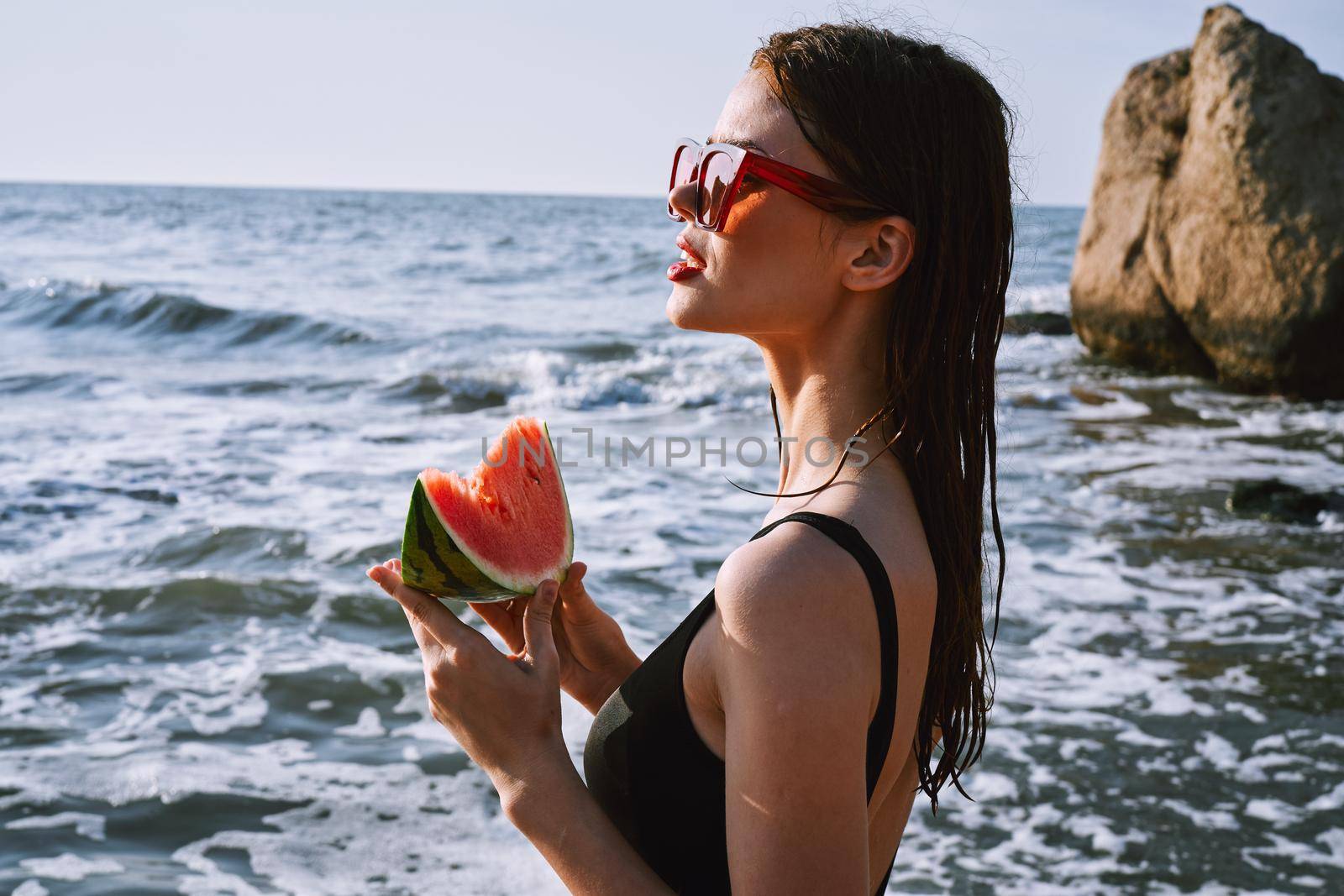 woman in black swimsuit with watermelon by the ocean. High quality photo