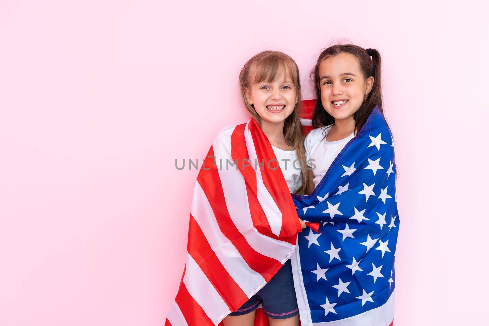 Amazed little kids girls showing white t-shirt, isolated on pink background. Childhood lifestyle concept. Mock up copy space. Pointing index finger aside by Andelov13