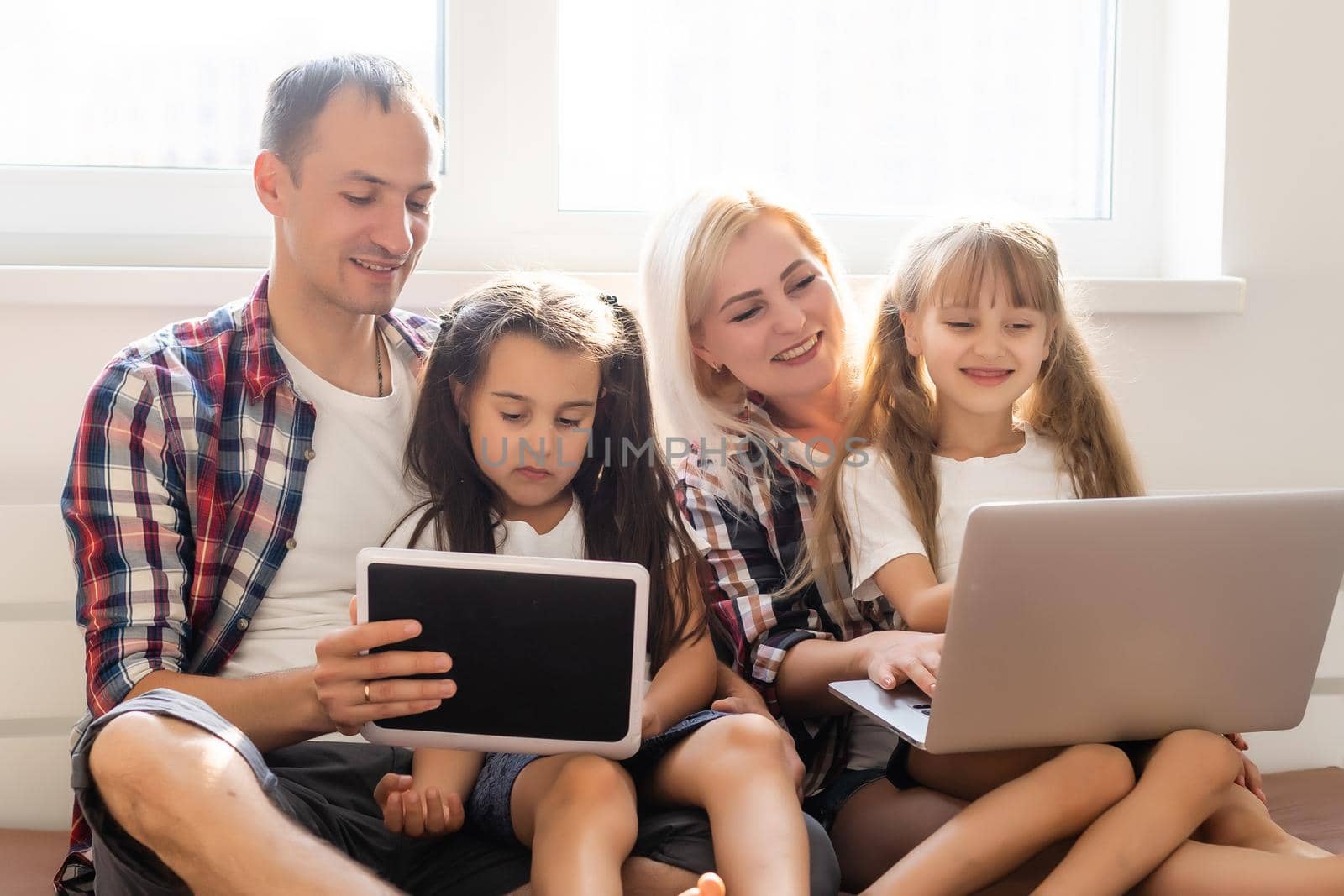 Happy family concept. Beautiful mother and handsome father with their daughters spending time together at home and lying on bed with laptop.