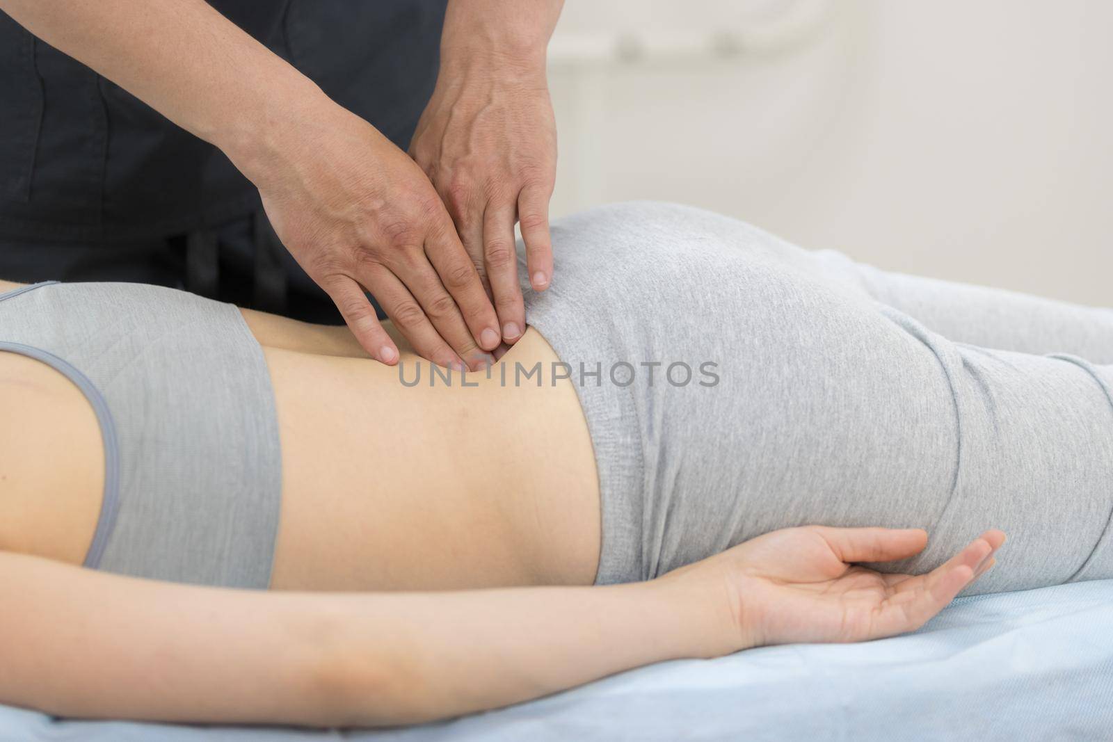 Young woman having osteopathy treatment - giving a massage on the loin. Mid shot