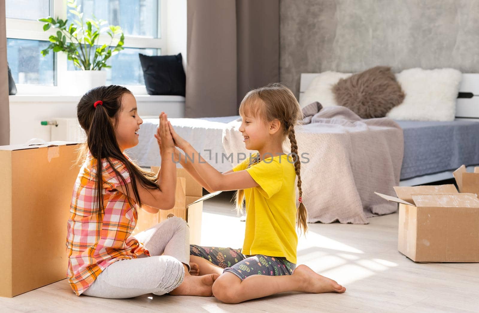 Happy family in living room. Preschool daughters sitting and help unpacking cardboard boxes belongings. Buy real estate, relocation at new modern house