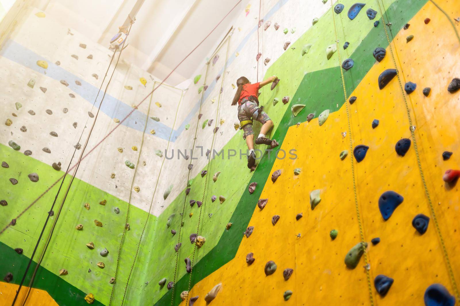 Sporty little girl climbing artificial boulder on practical wall in gym