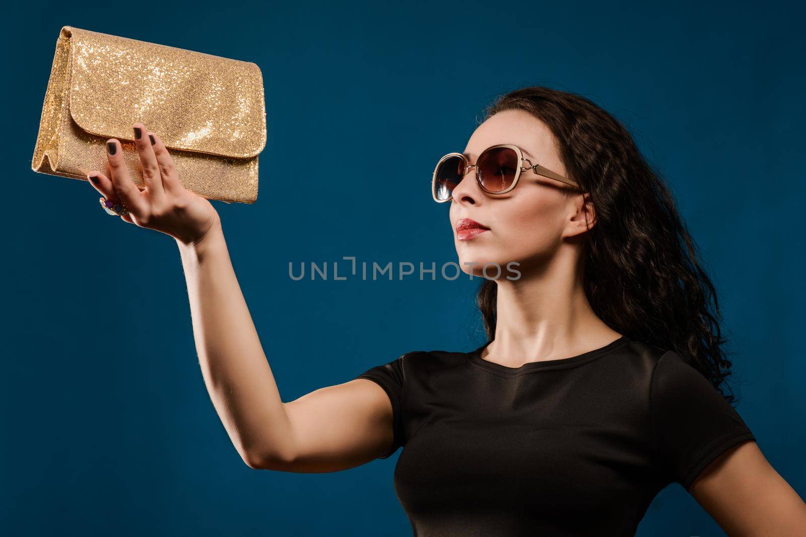 beautiful girl in a black dress with a golden clutch on blue background