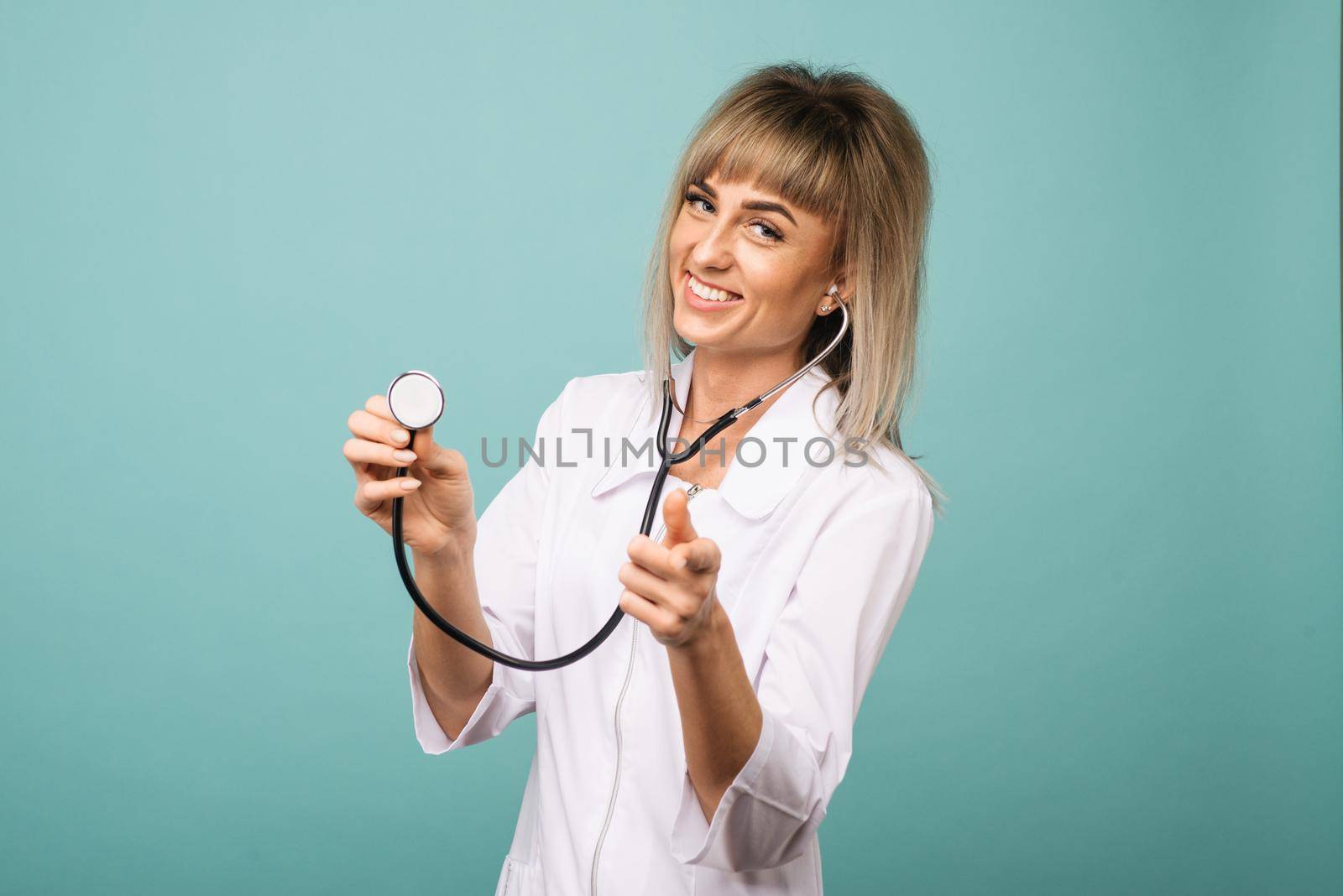 Young female doctor with stethoscope on foreground. Cut out of face isolated on blue background