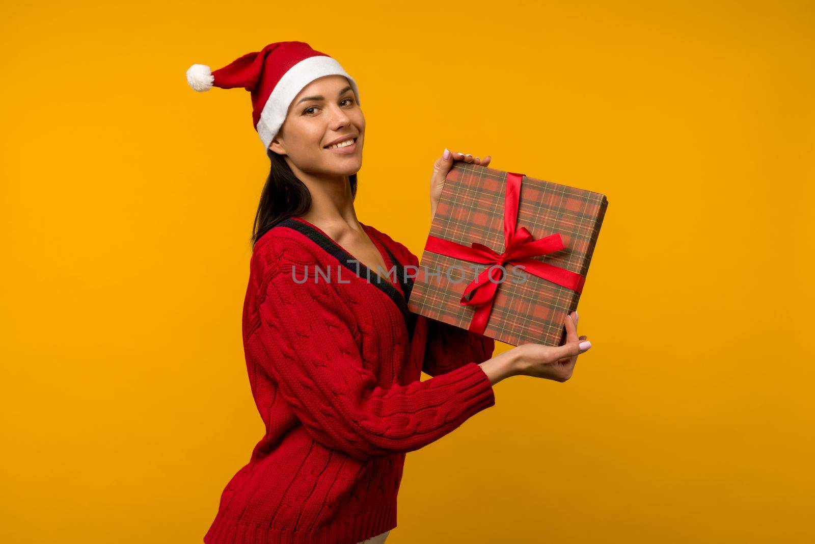 Happy excited young woman in santa claus hat with gift box over yellow background - image