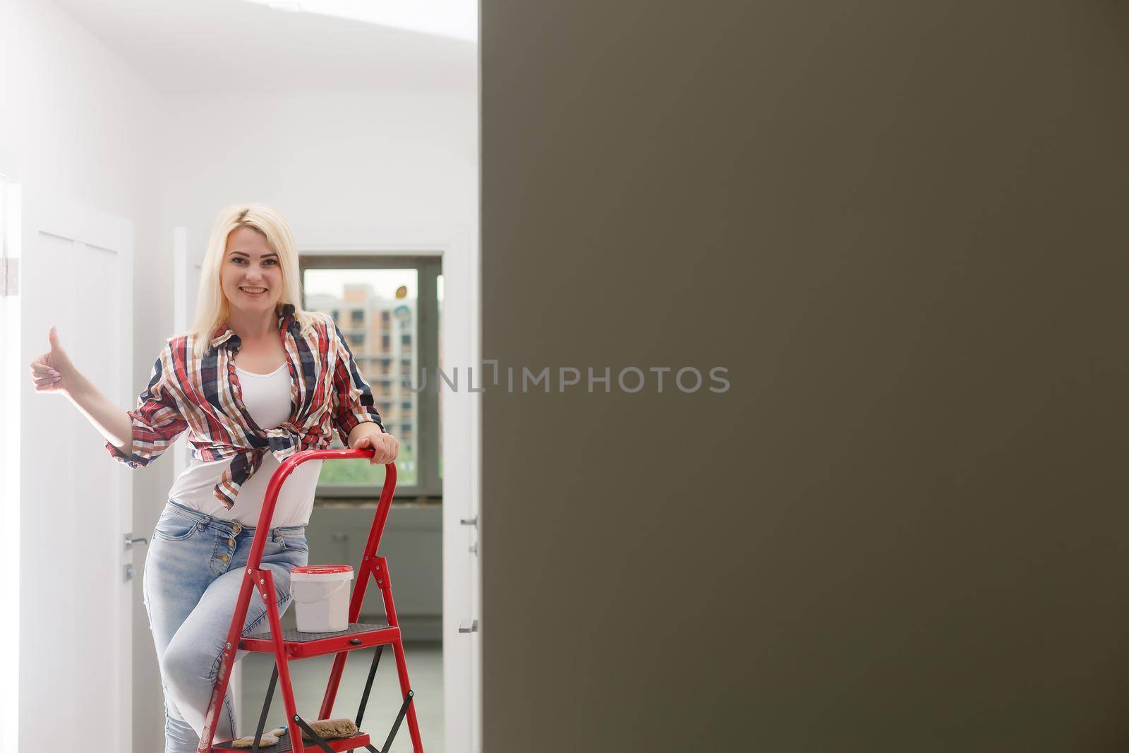 Beautiful young woman painting wall in room