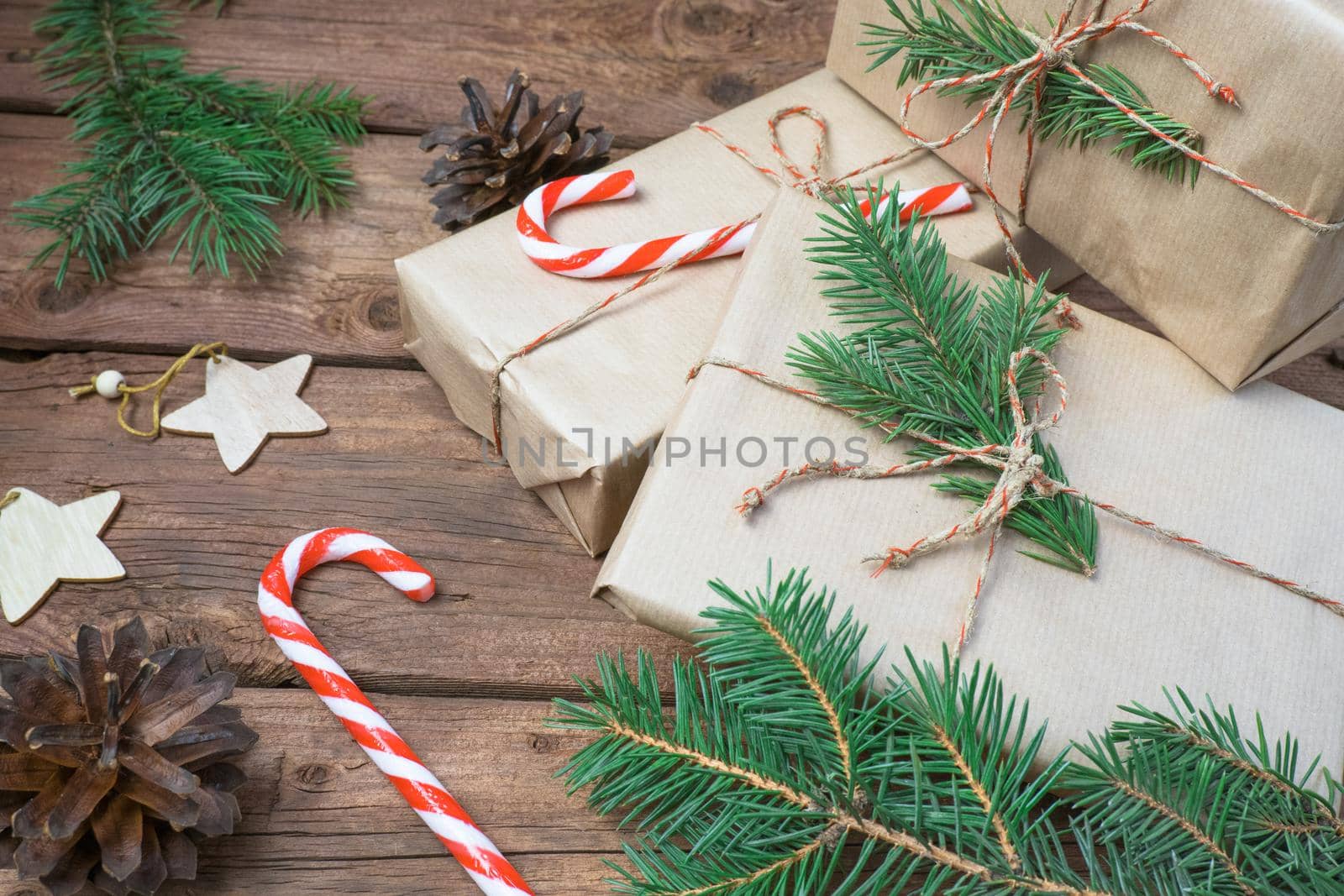 Christmas gifts or gift box wrapped in kraft paper with decorations, pine cones and fir branches on a rustic wooden background. by Ekaterina34