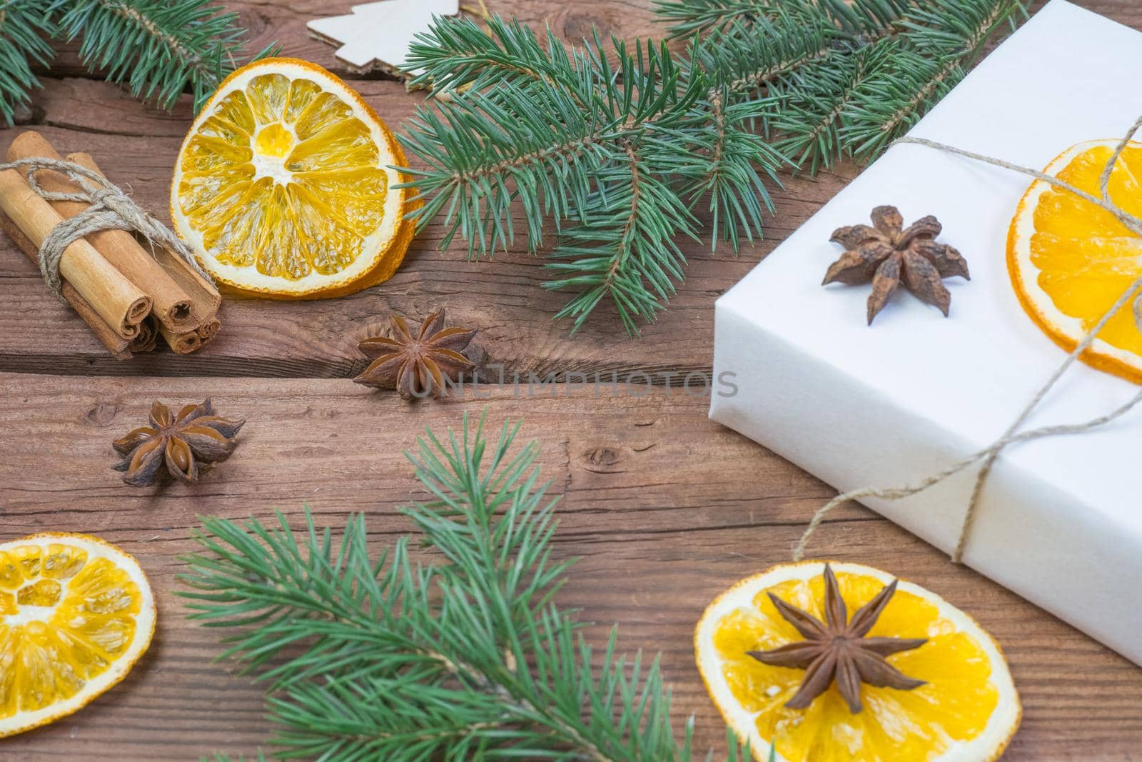 Christmas presents or gift box wrapped in kraft paper with decorations, pine cones, dry orange orange slices, cinnamon and fir branches on a rustic wooden background. Holiday concept