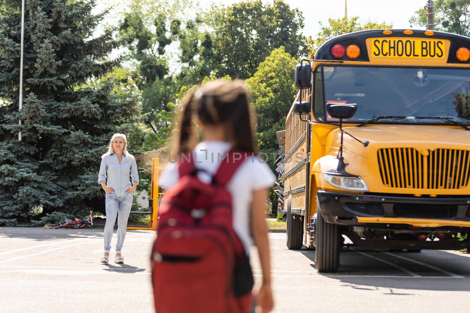 Mother escorts the schoolgirl with ponytails and a backpack to school. by Andelov13