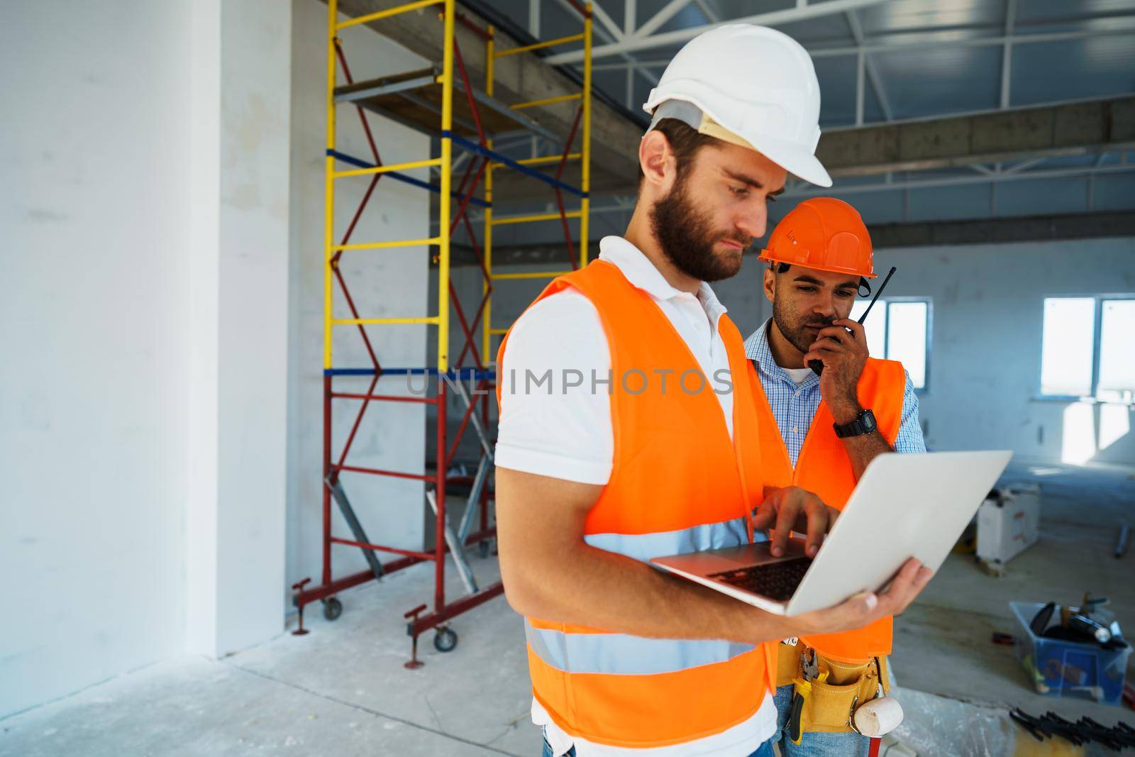 Two specialists supervisors in hardhats using laptop at construction site for work, close up