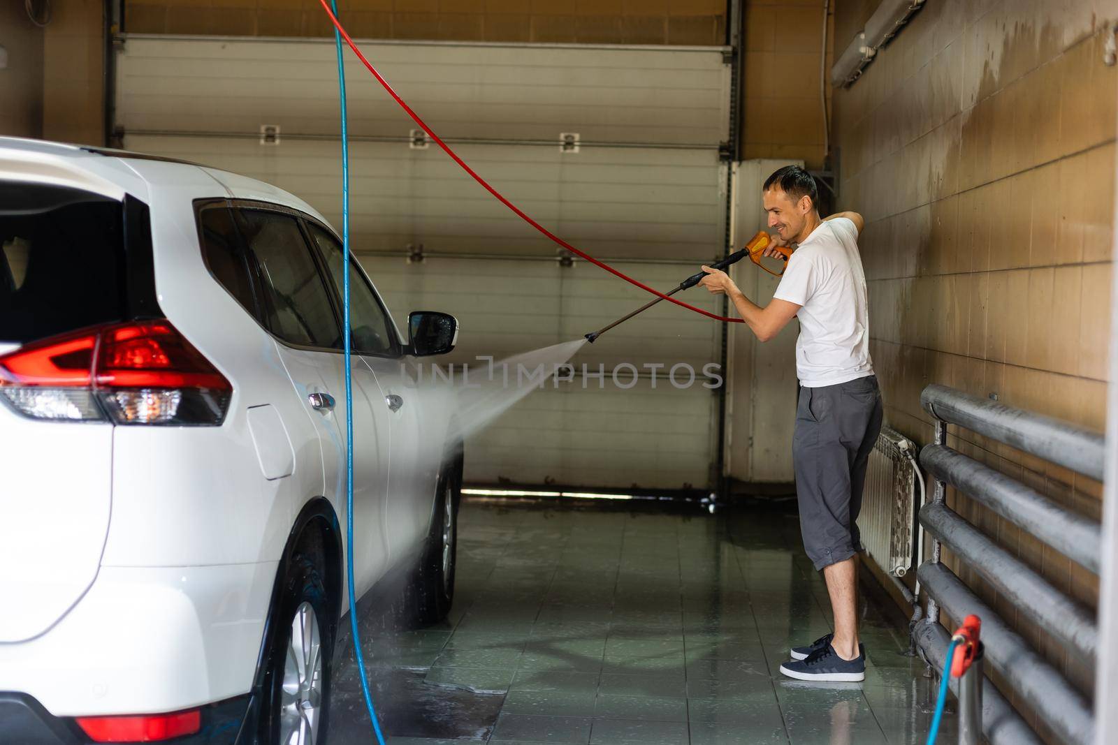 Young tall man spalshing his car by garden hose