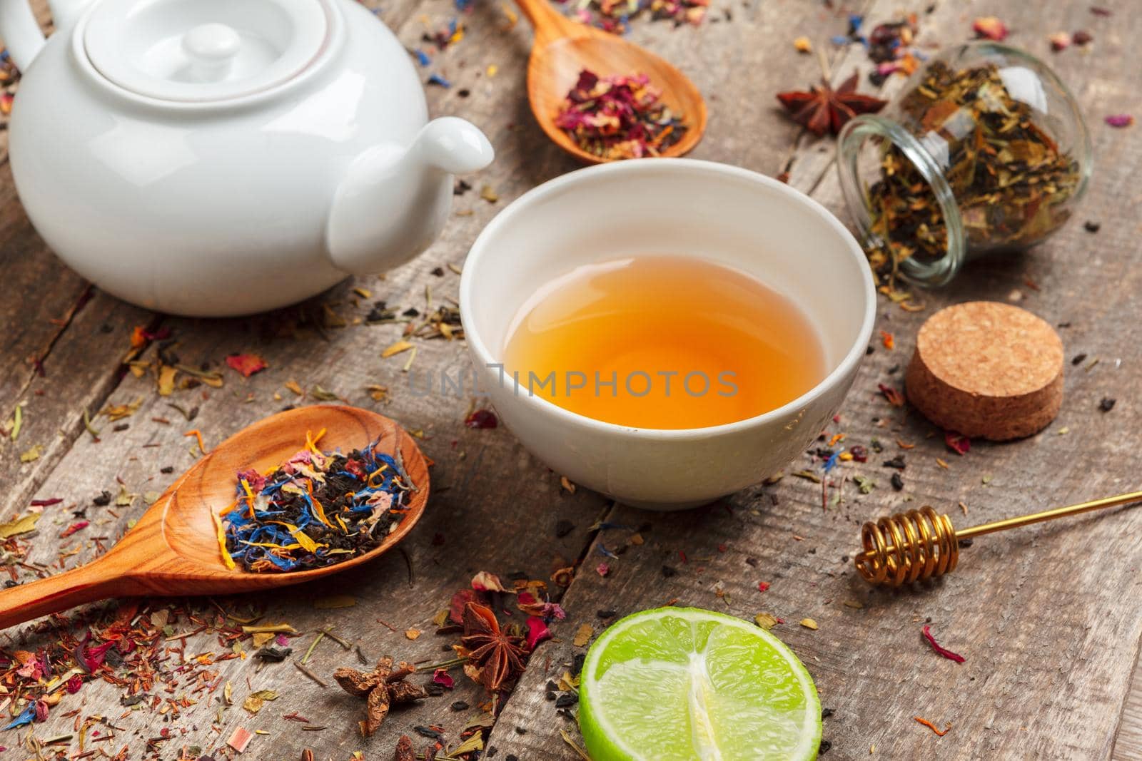 cups of healthy herbal tea with cinnamon, dried rose and camomile flowers in spoons over wooden background, top view