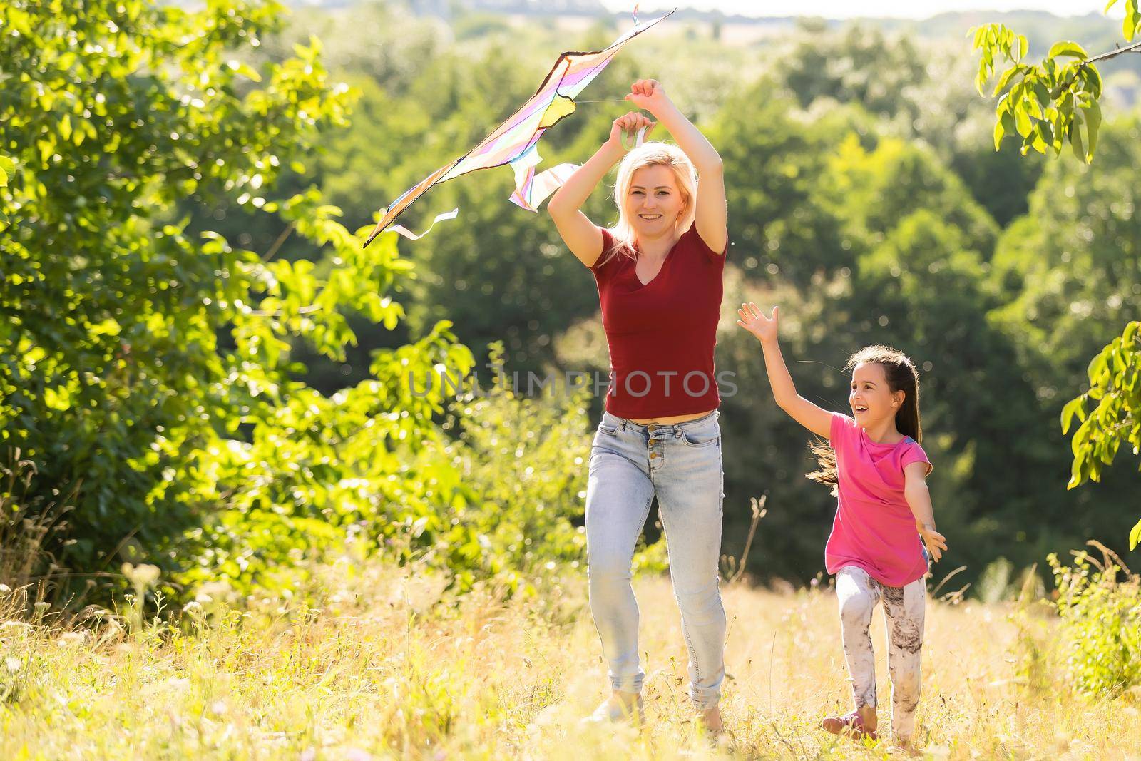 happy family mother and child run on meadow with a kite in the summer on the nature