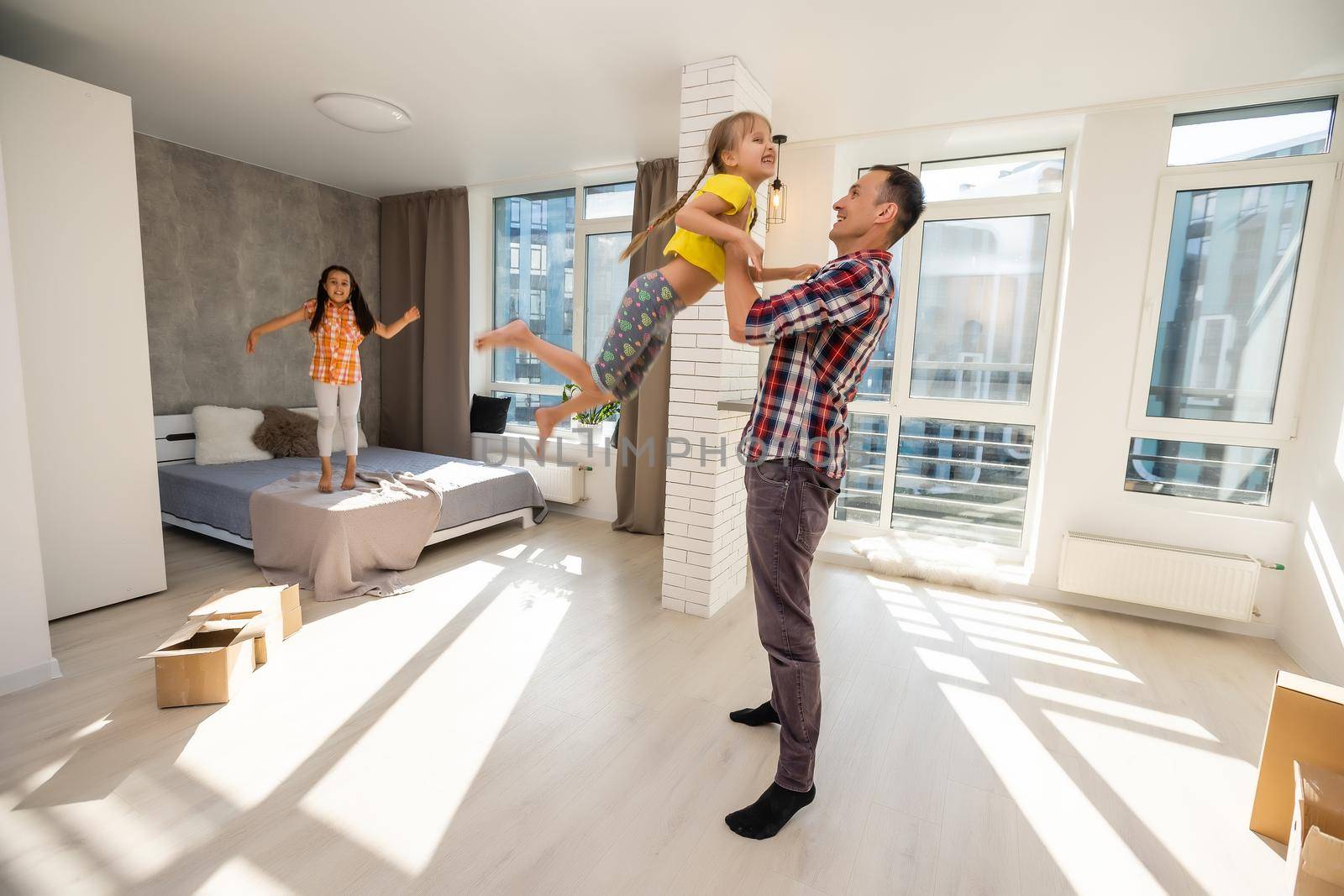 Overjoyed young father holding two little children siblings, having fun together at home, head shot. Excited dad playing with joyful adorable small daughter sisters, enjoying tender weekend moment.