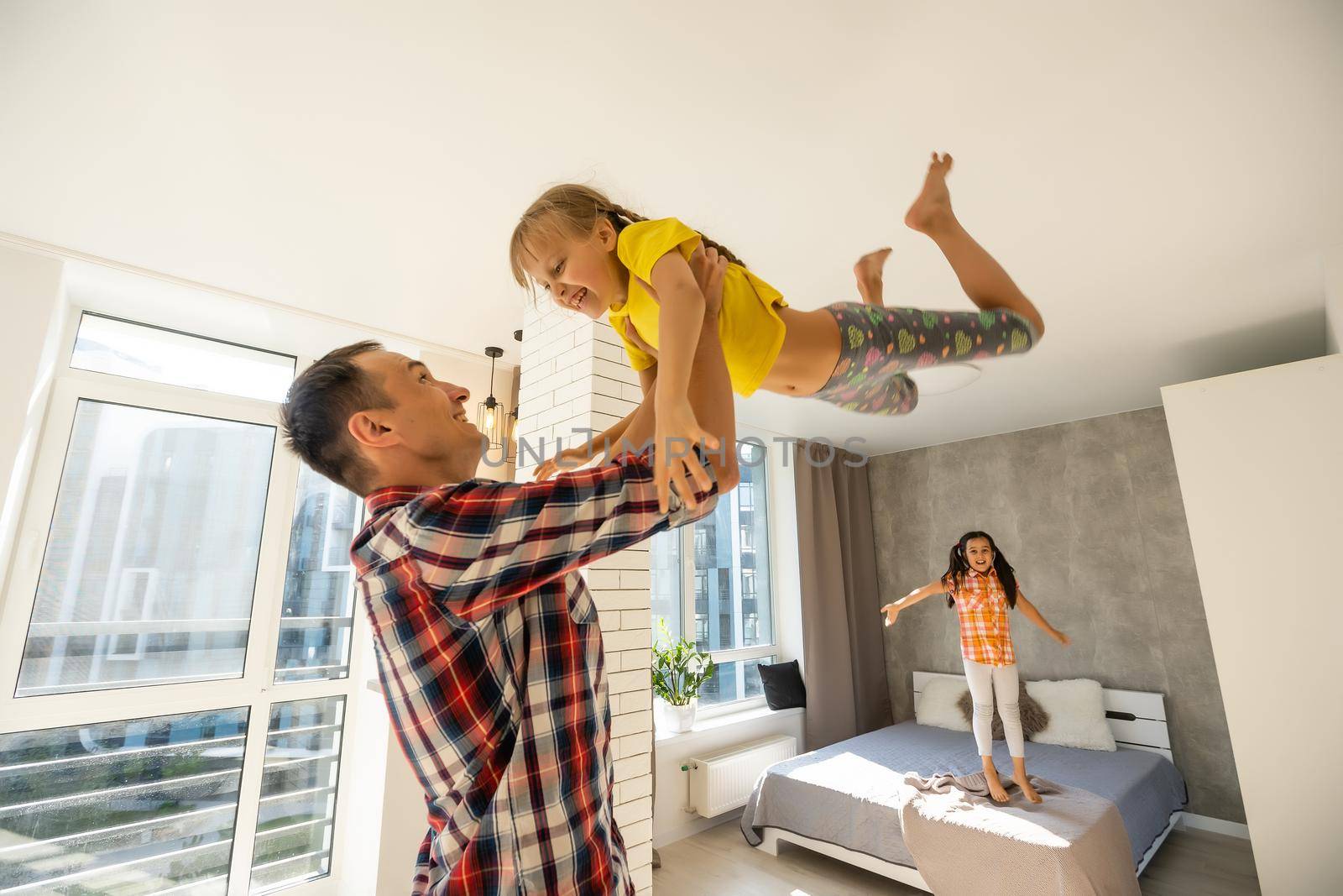 Overjoyed young father holding two little children siblings, having fun together at home, head shot. Excited dad playing with joyful adorable small daughter sisters, enjoying tender weekend moment.