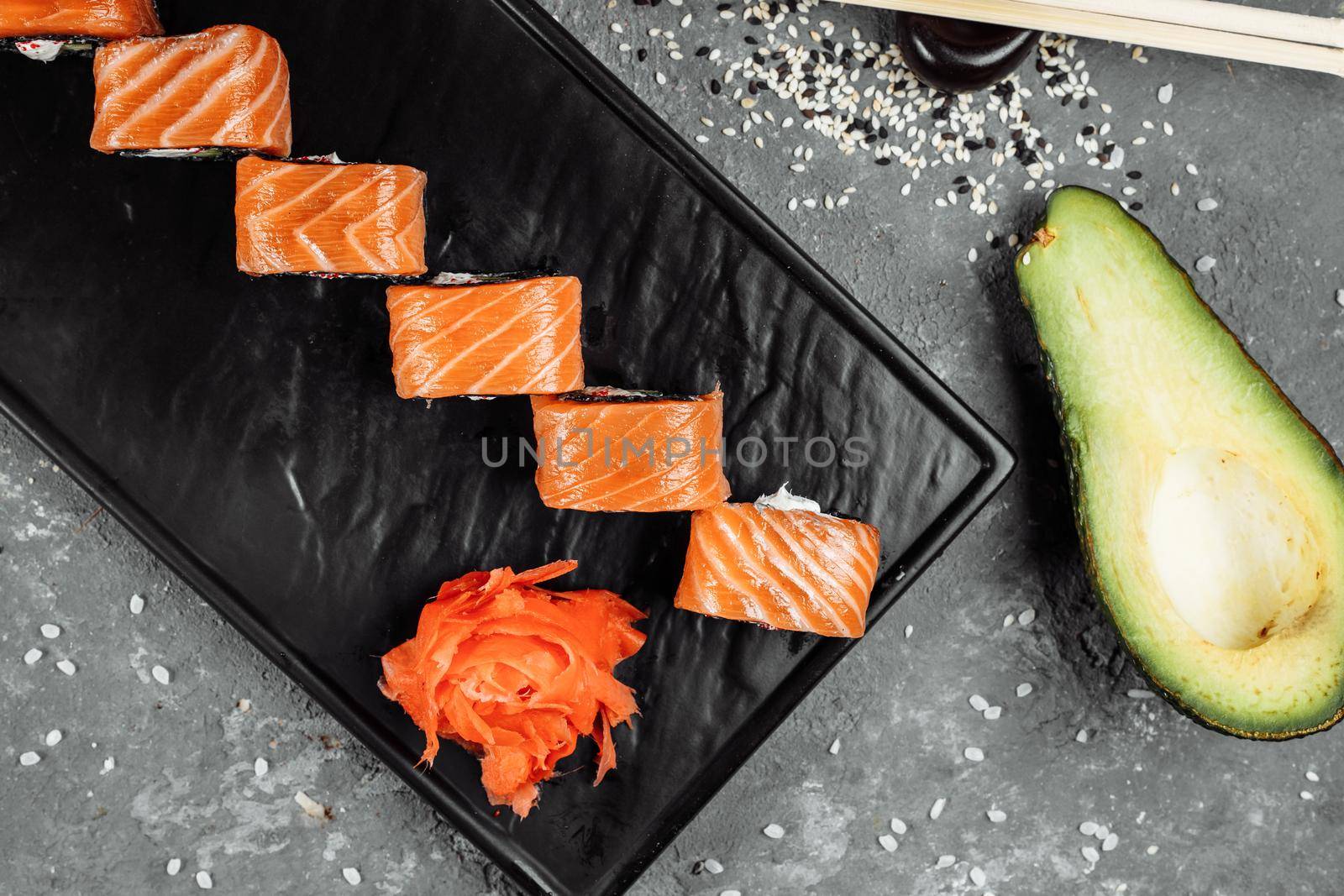 A set of sushi rolls Philadelphia with red fish, cream cheese and black rise lies in a plate boat. Sushi rolls on a gray background.