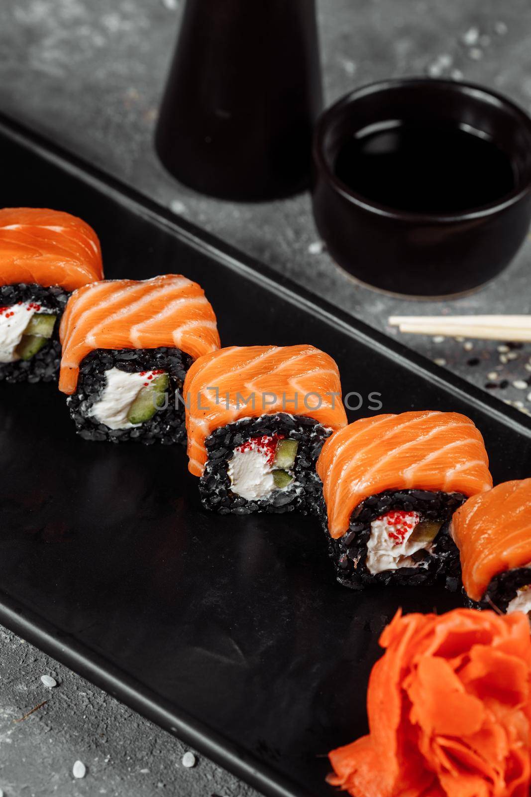 A set of sushi rolls Philadelphia with red fish, cream cheese and black rise lies in a plate boat. Sushi rolls on a gray background.