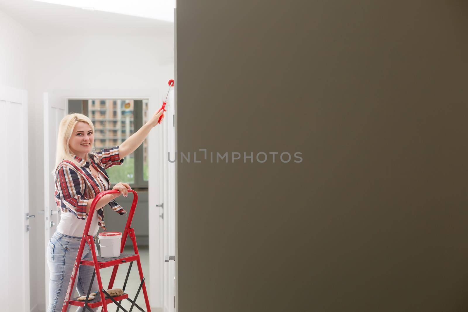 Beautiful young woman painting wall in room