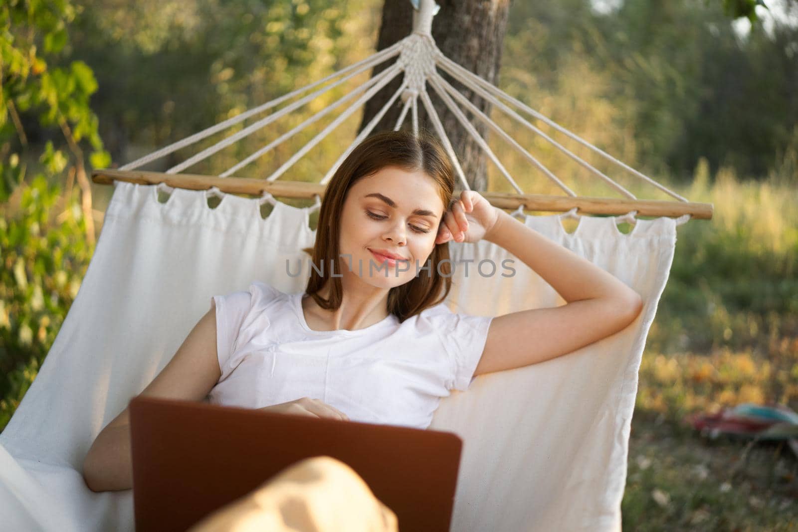 cheerful woman lies in a hammock with a laptop vacation internet travel. High quality photo