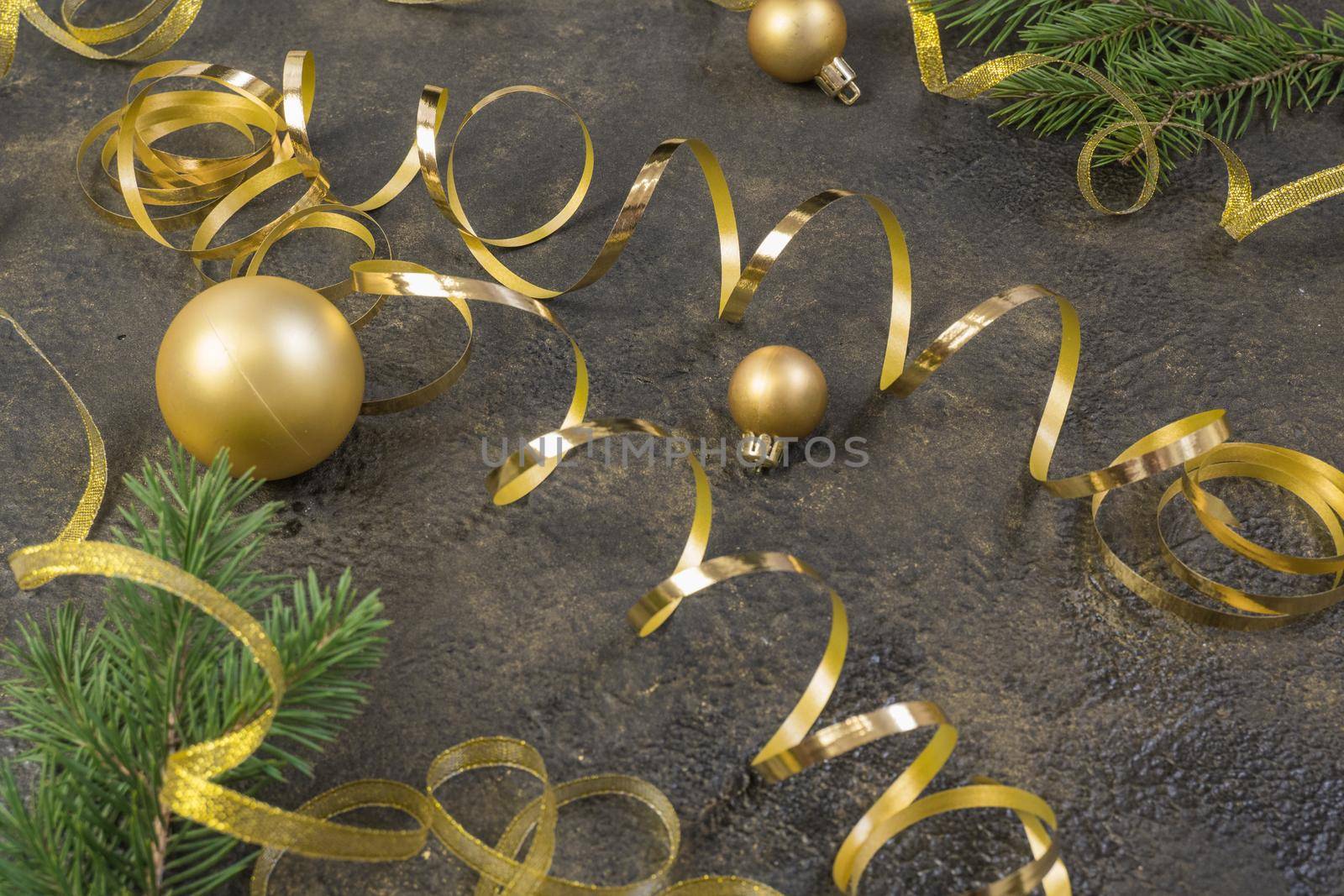 Christmas composition of yellow Christmas balls, fir branches and a gold ribbon on a black with gold embossed background