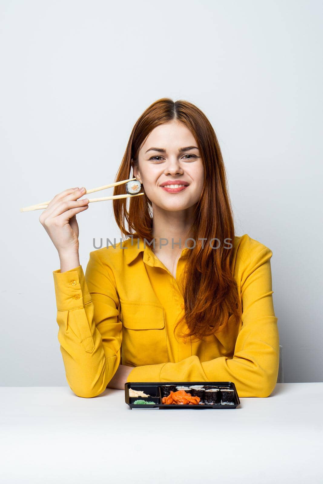 a woman in a yellow shirt sits at a table and eats sushi. High quality photo