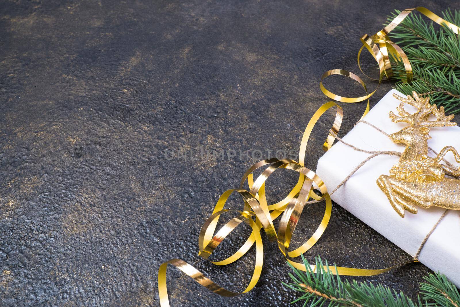 Christmas composition of fir branches, gold ribbon, gift box in craft paper on black with gold embossed background with place for text