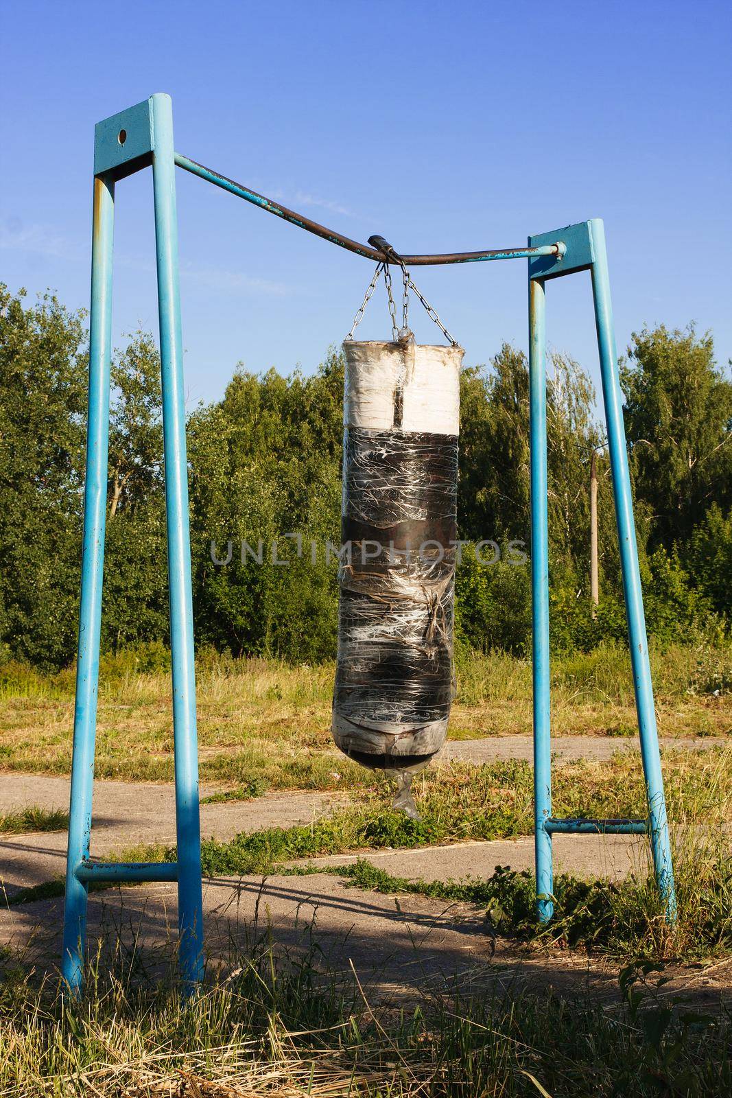 old punching bag hangs on a bar on an abandoned sports ground by zartarn