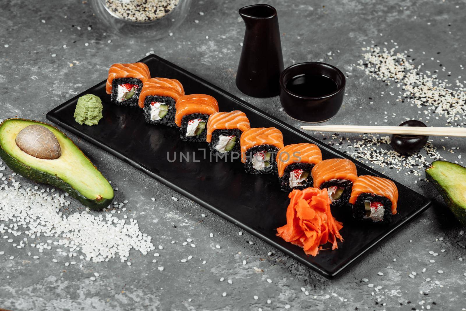 A set of sushi rolls Philadelphia with red fish, cream cheese and black rise lies in a plate boat. Sushi rolls on a gray background.