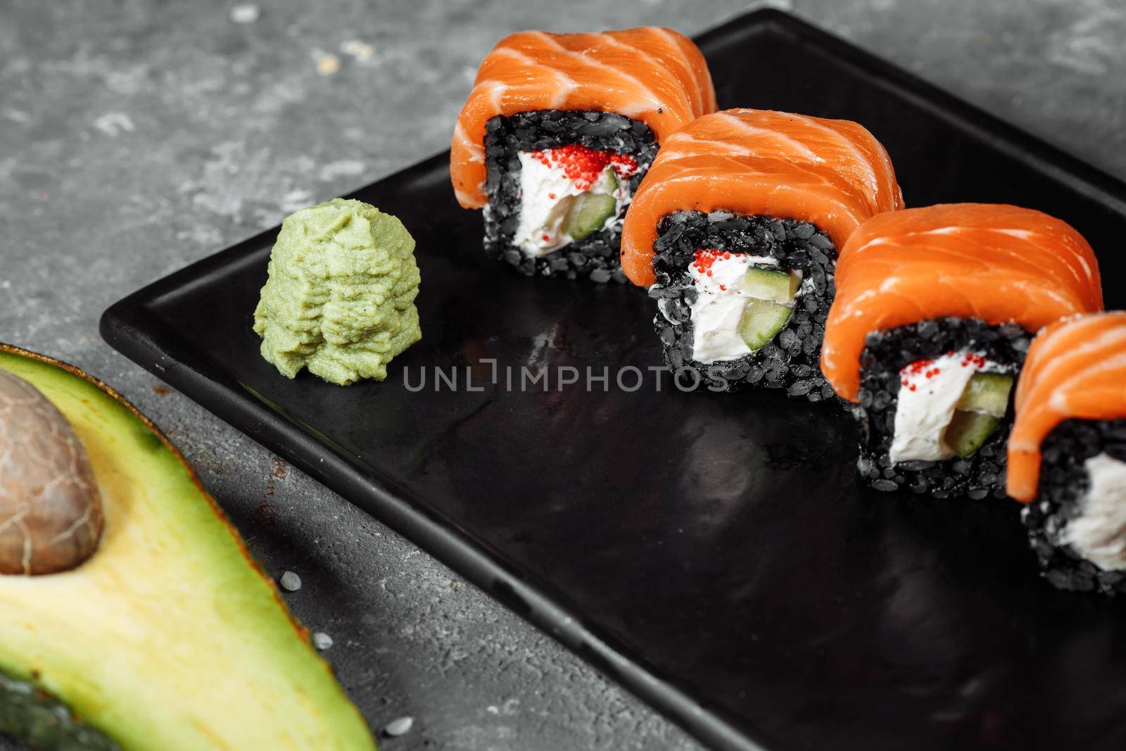 A set of sushi rolls Philadelphia with red fish, cream cheese and black rise lies in a plate boat. Sushi rolls on a gray background.