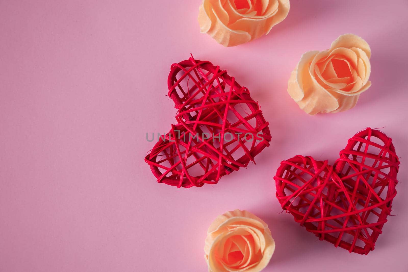 Red hearts and orange rosebuds on a pink background. Concept for Valentine's Day. Place for text.