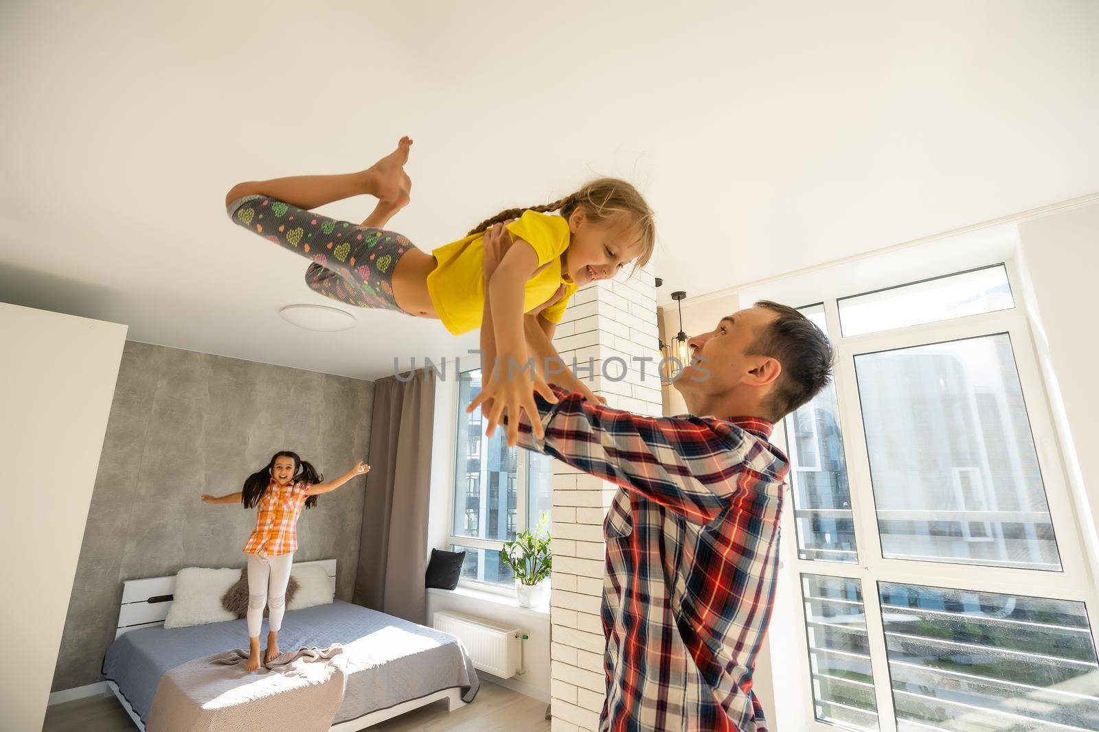 Overjoyed young father holding two little children siblings, having fun together at home, head shot. Excited dad playing with joyful adorable small daughter sisters, enjoying tender weekend moment.