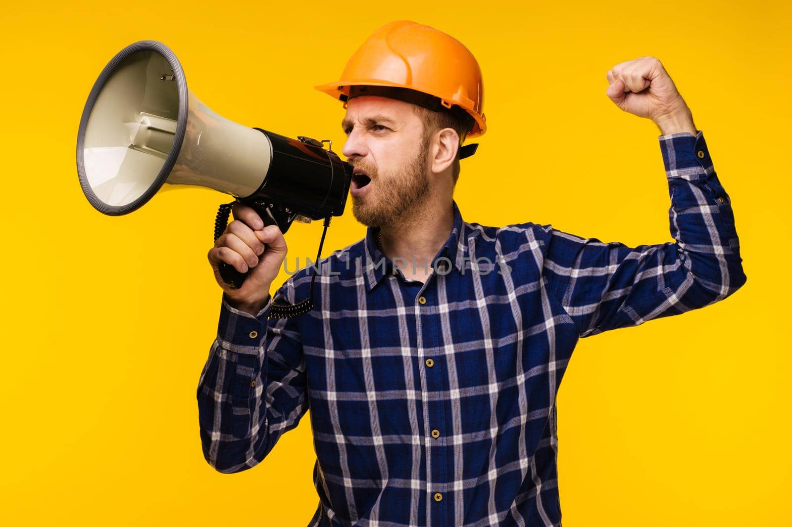 Angry worker man in orange helmet with a megaphone on yellow background - Image